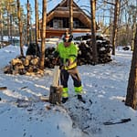 Mies pilkkoo puita kirveellä suuren runkopinon edessä