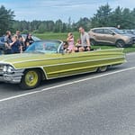 lapsetkyydissä Kellanvihreä avoauto ajaa yleisön editse. Lapset seisovat takapenkillä