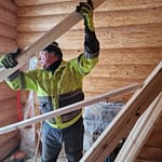 Mies nostaa lautoja ylös. Taustalla pyöröhirsiseinä