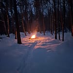 Nuotiotuli lumisessa metsässä iltahämärissä