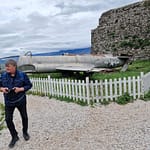 Lentokone valkoisen aidan takana. Etualalla mies kameran kanssa