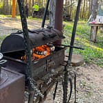 Suuressa grillissä kansi raollaan ja makkaroita tulella