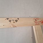 laudan päällä poikittaislauta ja naula, jonka päälle on piirretty kuva ja nimi