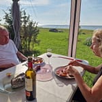 Mies ja nainen ruokailevat paviljonkiteltassa meren rannalla