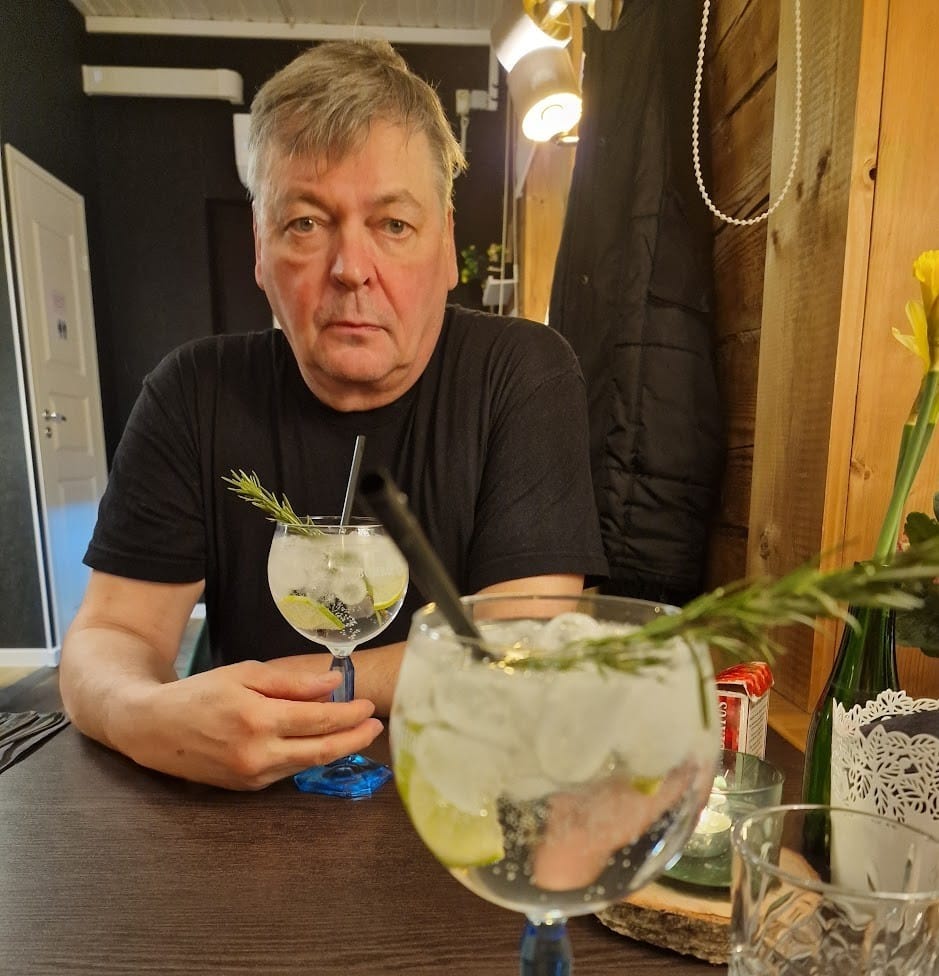 aperitiivi Ravintolan pöydässä kaksi rosmariinilla koristettua gin tonicia jalallisessa lasissa. Taustalla väsyneen näköinen mies